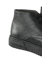 Close-up of black leather ankle boot with lace, stitching, and thick sole.