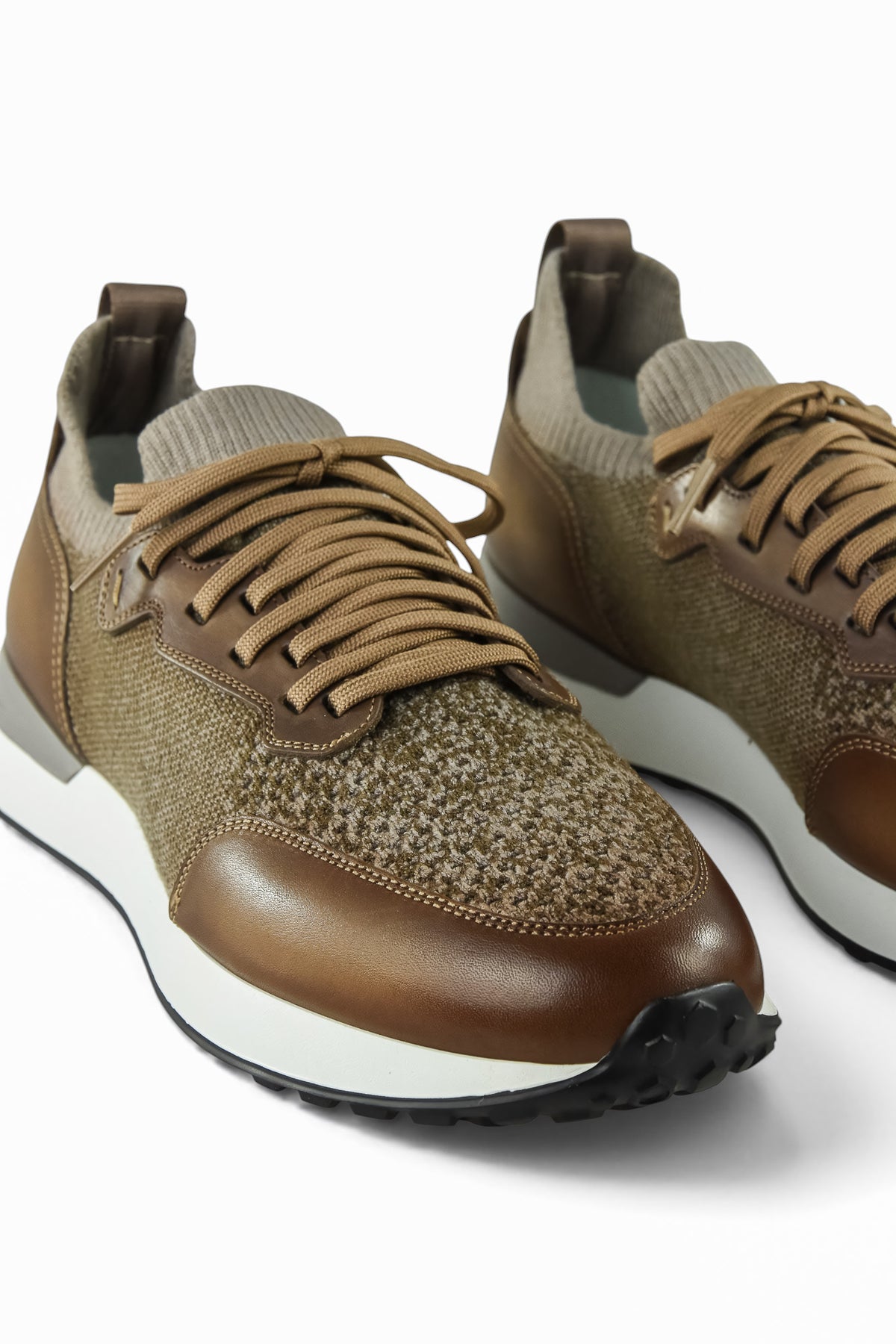 Two tan lace-up trainers showing knit uppers, brown leather toe trim, and white soles