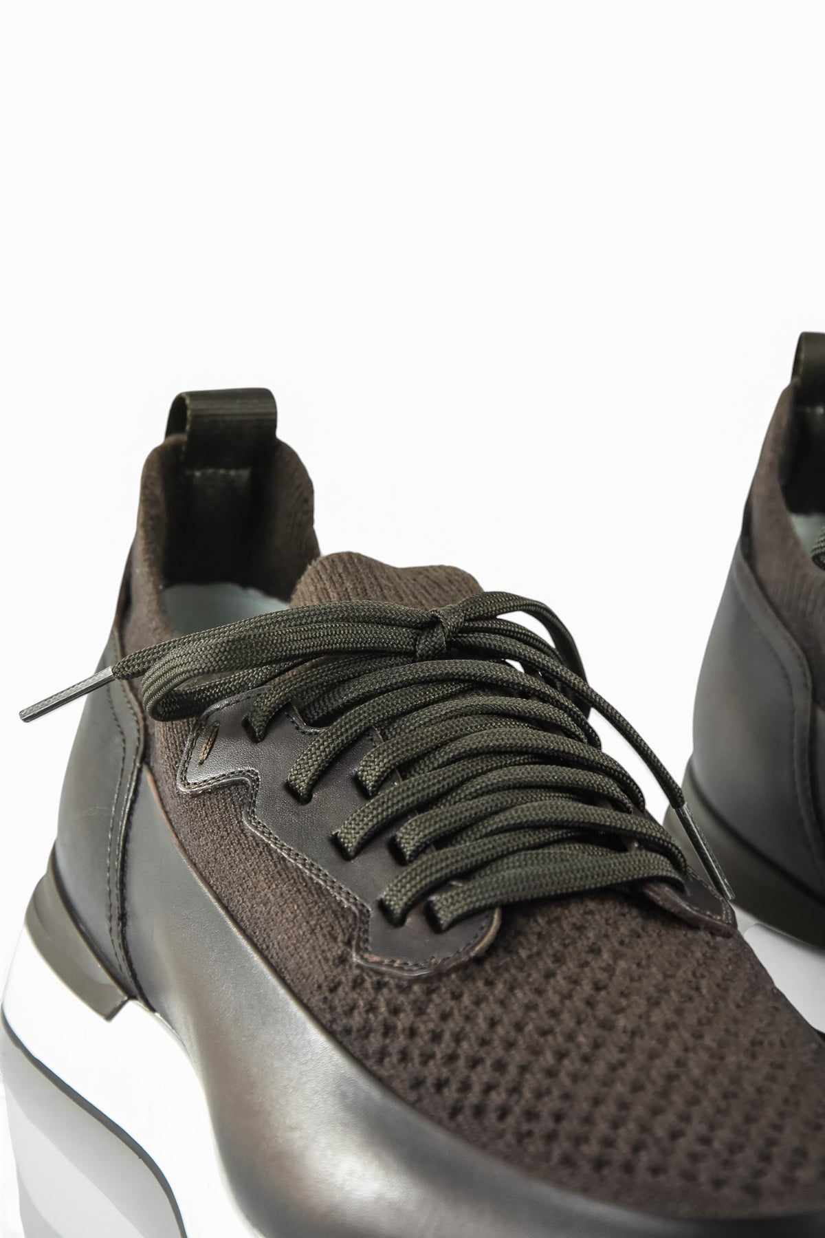 Close-up of dark brown lace-up trainer with knit upper and leather side panel.