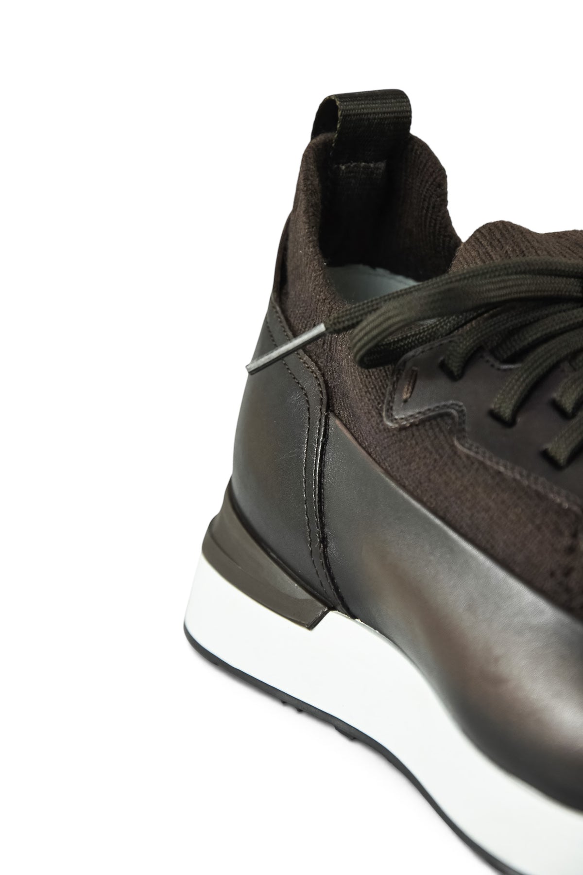 Close-up of dark brown lace-up trainer heel and side leather panel with knit texture.