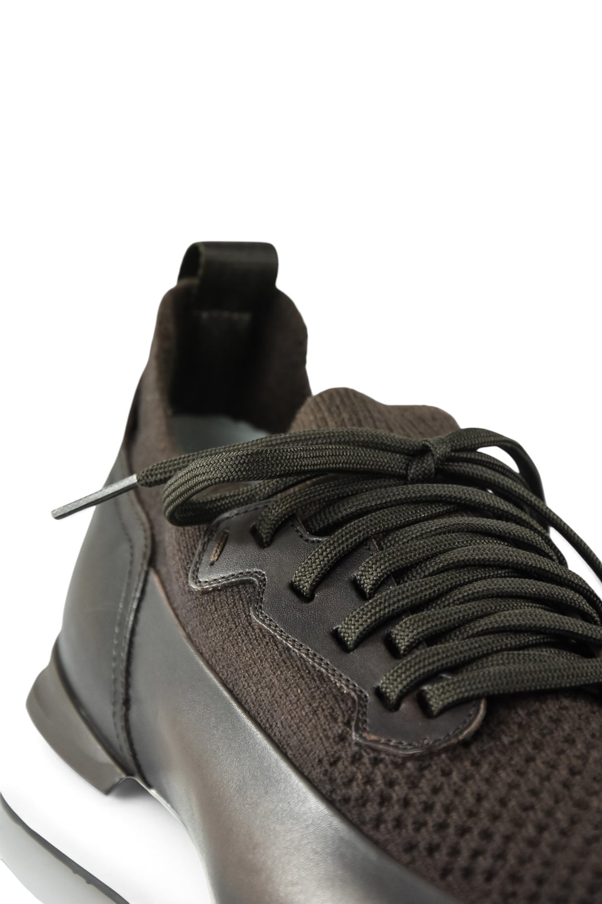 Close-up front quarter of dark brown lace-up trainer with knit upper and white sole.