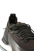 Close-up front quarter of dark brown lace-up trainer with knit upper and white sole.