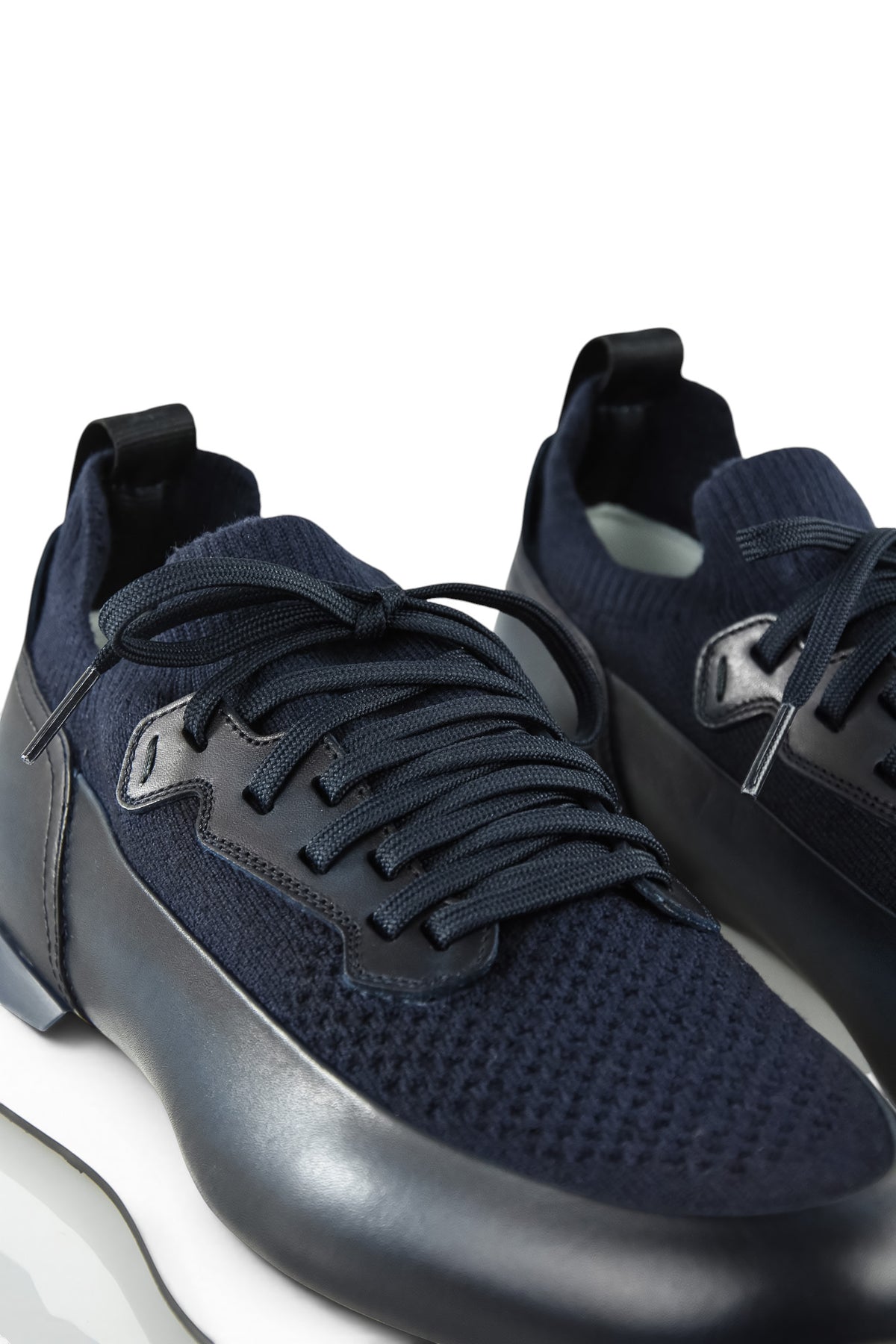 Close-up of dark blue trainers showing knit toe, leather overlays, and lace-up details