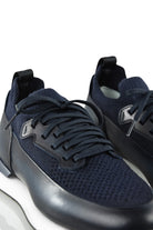 Close-up of dark blue trainers showing knit toe, leather overlays, and lace-up details