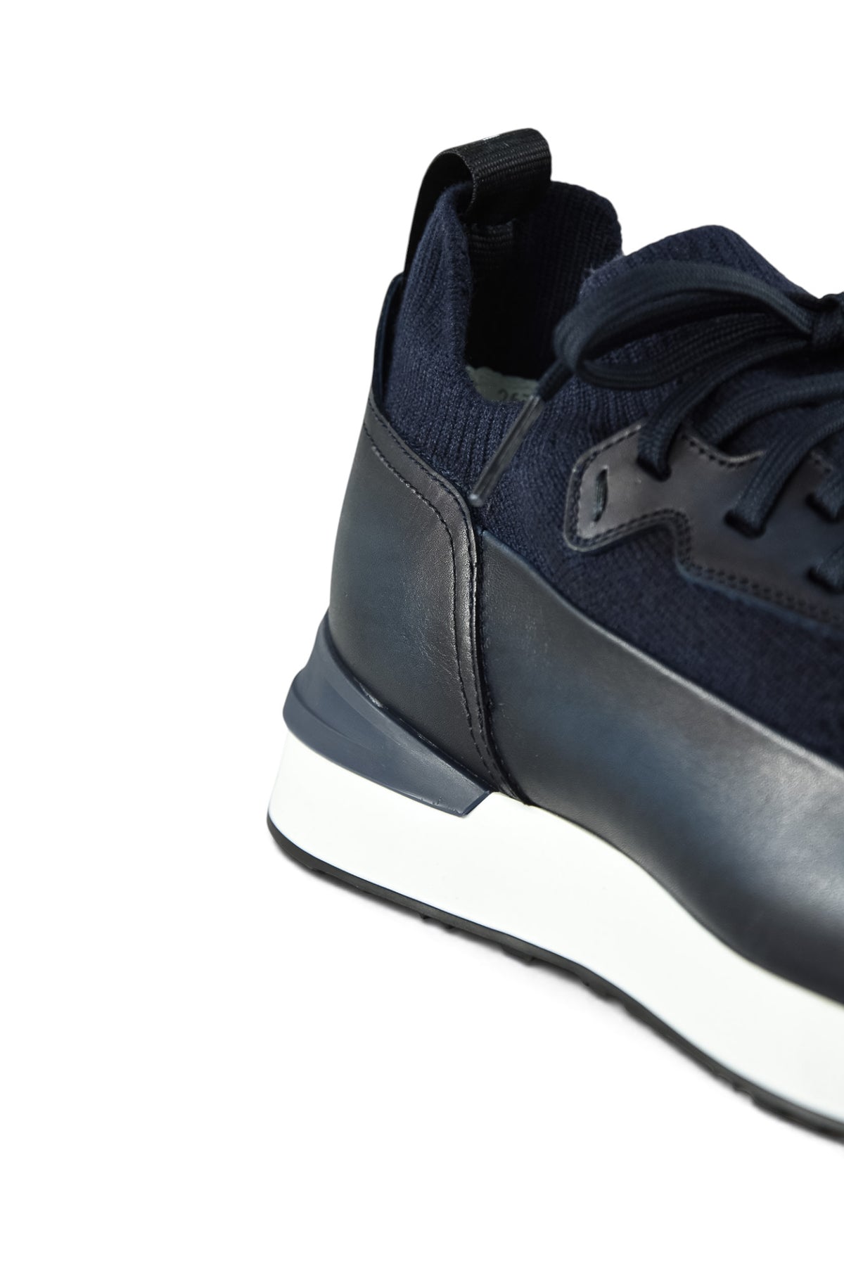 Close-up heel of dark blue trainers with knit collar, leather side, and white rubber sole