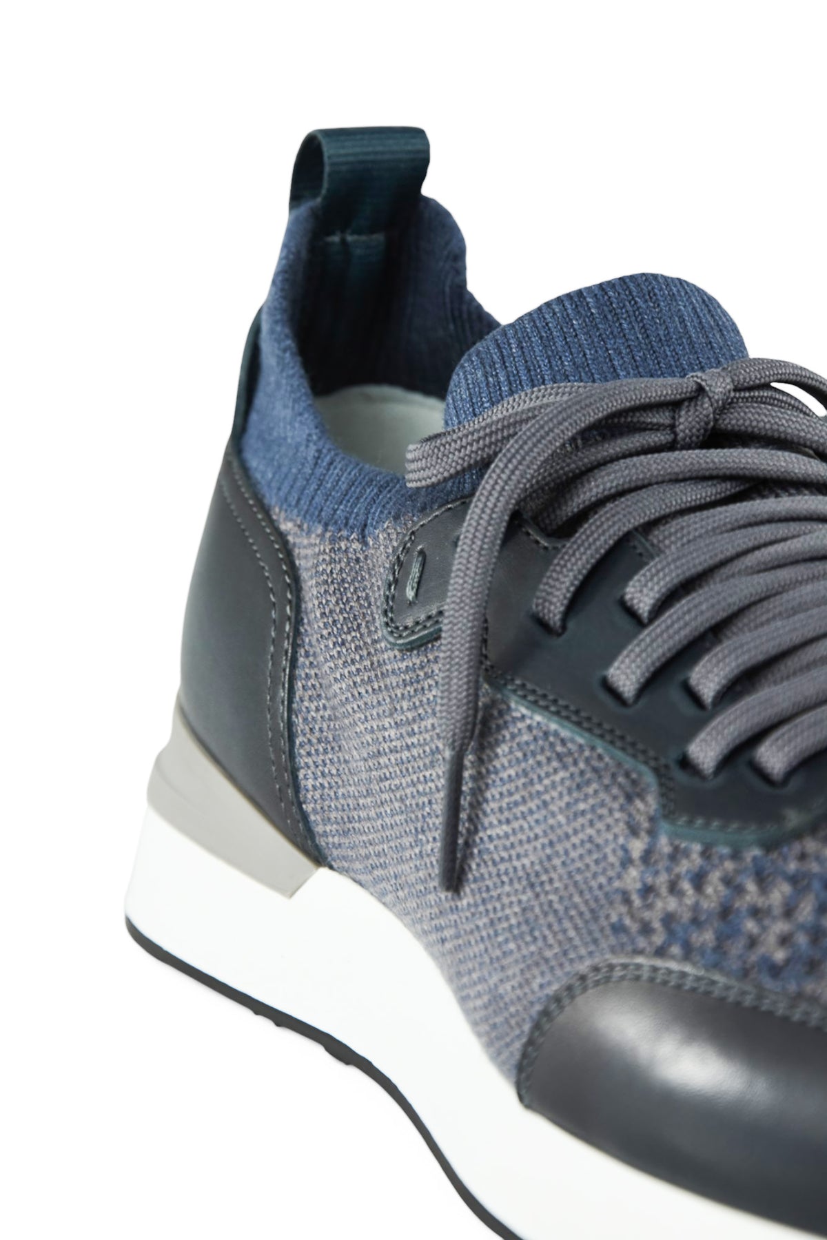 Close-up of men's trainer quarter: grey knit upper, dark leather lace panel, side view