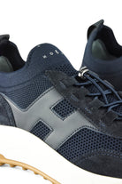 Navy trainer sneaker close-up with perforated knit panels and silver lace eyelets
