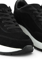 Close-up of black suede lace-up trainers with white midsole and tread