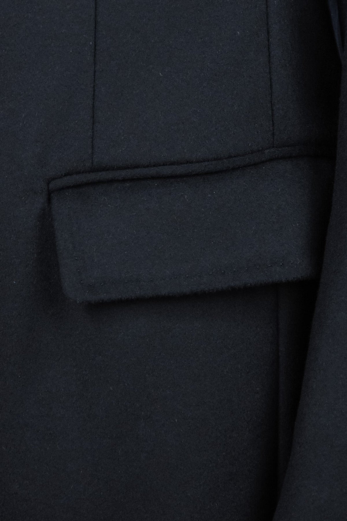 Dark wool and cashmere overcoat detail showing a flap pocket and vertical seam
