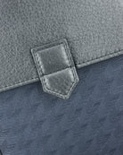 Blue flap hardware with square leather reinforcement patch and stitching on textured panel.