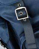 Nylon backpack strap attachment with metal square buckle and circular grommet; blue.