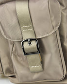 Beige backpack strap close-up with metal square buckle and stitched fabric tab.