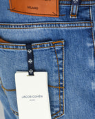 Men's stretch denim jeans detail: tan hang tag on belt loop, orange stitching