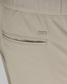 Taupe tech pants front detail: zip pocket and Herno logo patch.