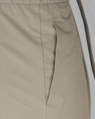 Taupe tech pants detail: side seam and front pocket on lightweight fabric.