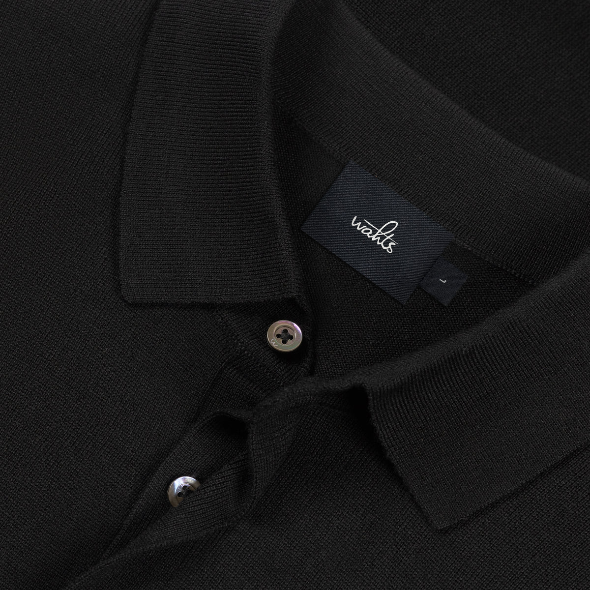 WAHTS black merino polo close-up of collar, placket buttons, and woven brand label
