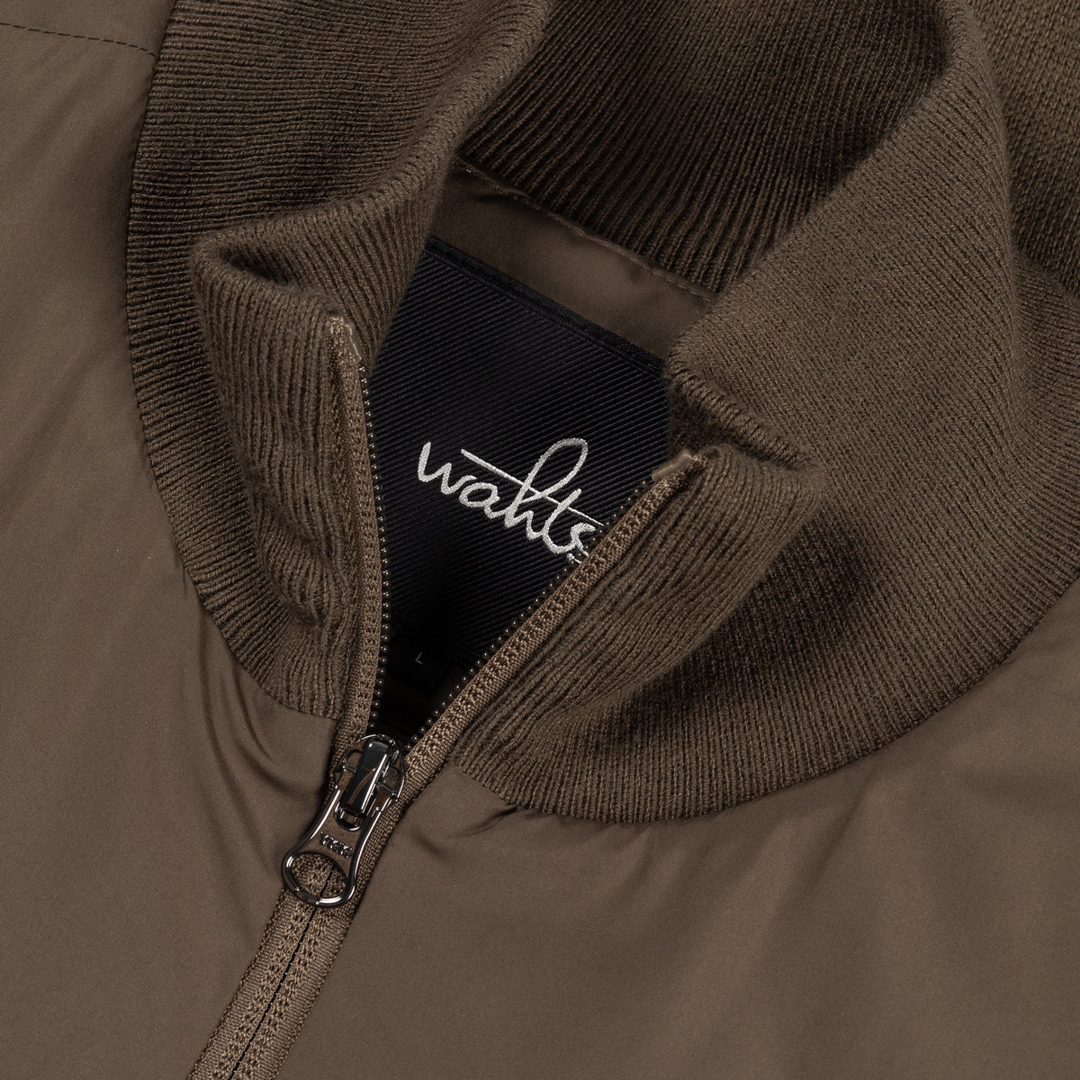 Close-up of wahts logo zipper on dark olive jacket with ribbed knit collar