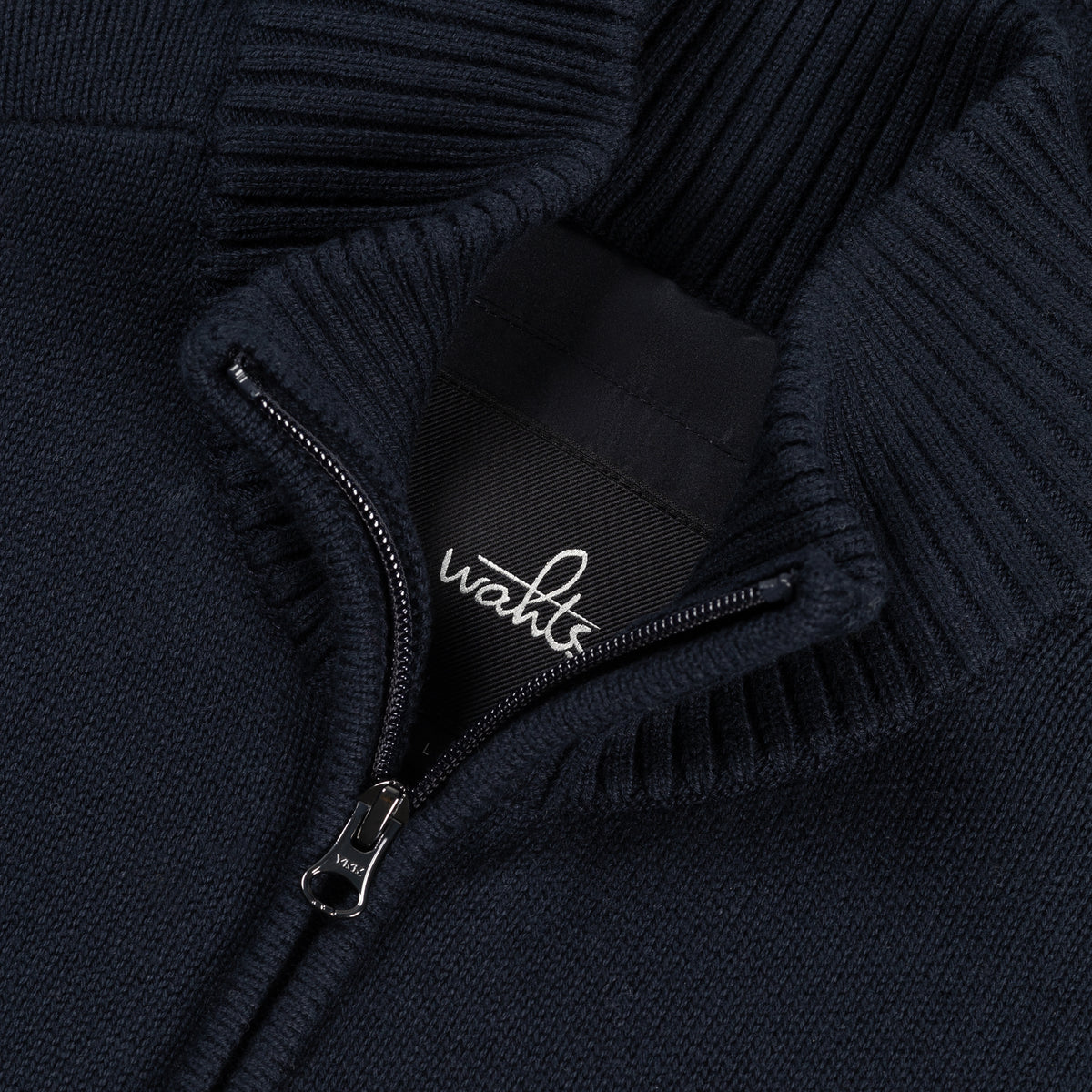 Full-zip cardigan close-up with branded zipper pull and ribbed knit cuffs