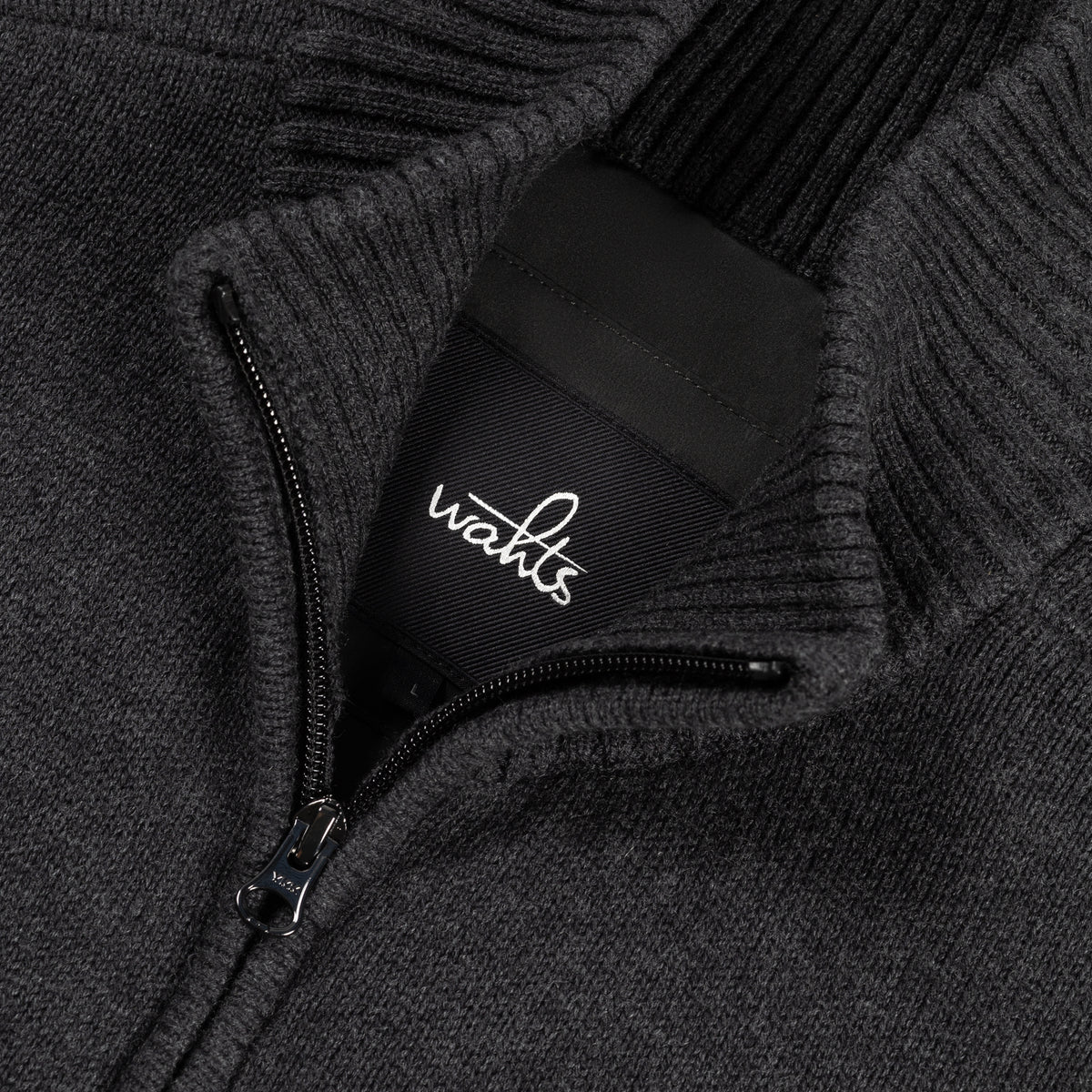 Black WAHTS logo patch on dark full-zip cardigan neck zipper detail