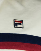 Cream jacket logo patch on chest with navy border and red accent.