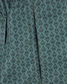 Teal swim shorts with repeating fleur monogram print, close-up of front panel