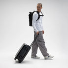 Person pulling a black hardshell suitcase with telescopic handle and wheels