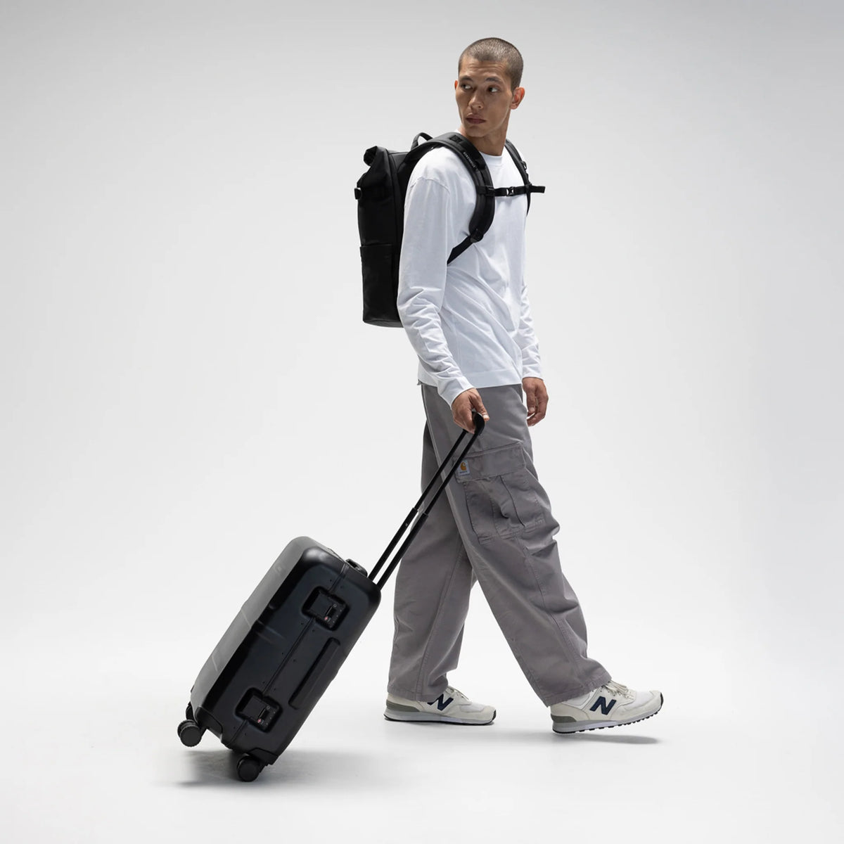 Person pulling a black hardshell suitcase with telescopic handle and wheels