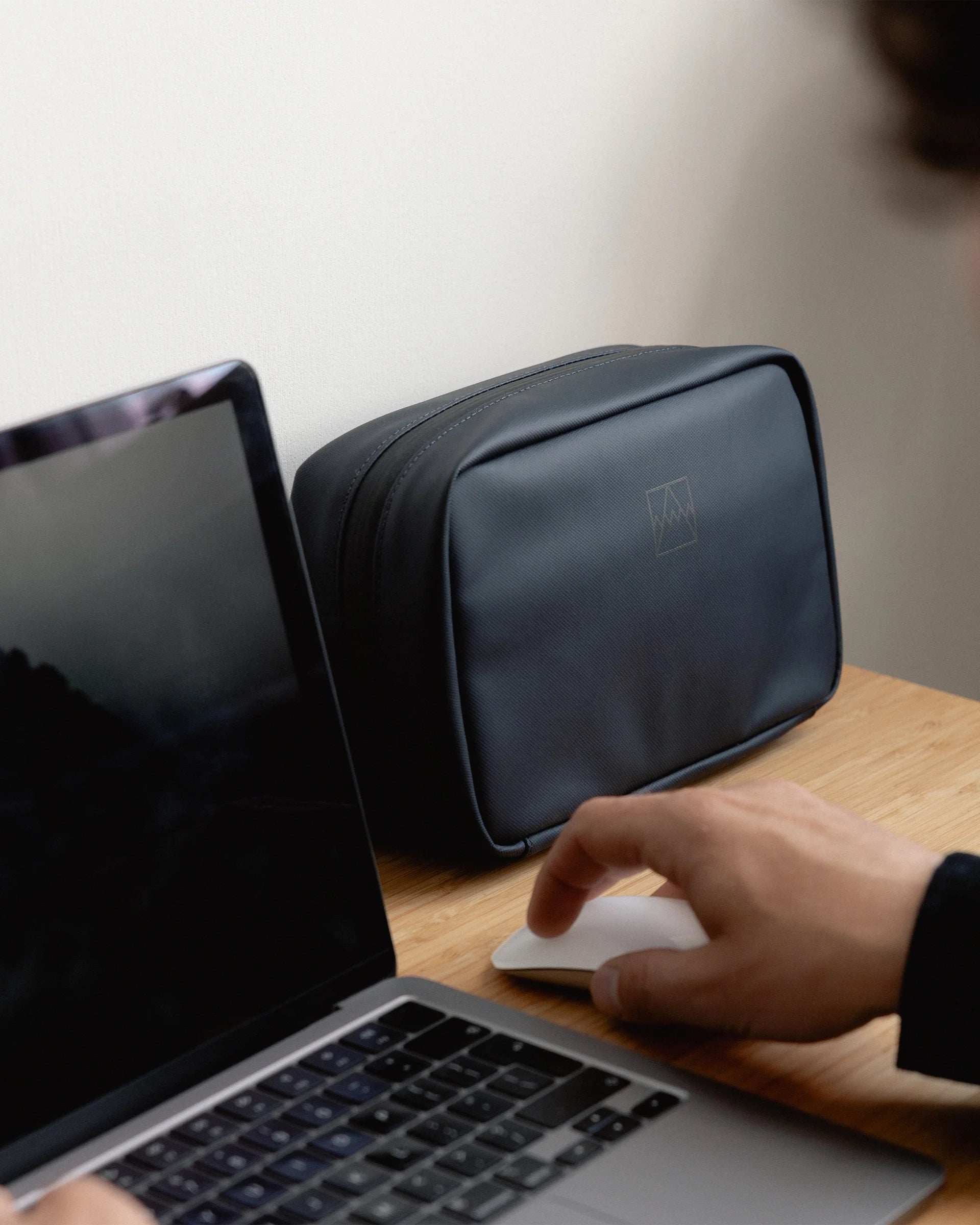 Waterproof tech bag in dark blue on a desk next to a laptop